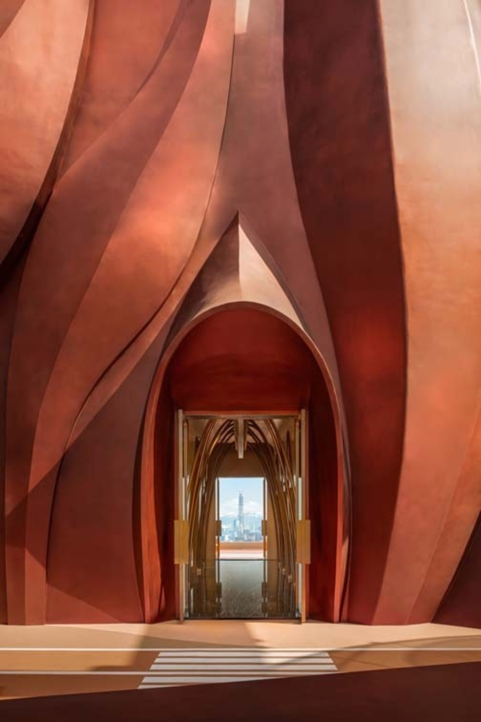 A dramatic interior with flowing, warm-toned walls leading to an inviting glass door that frames a city skyline in the background.