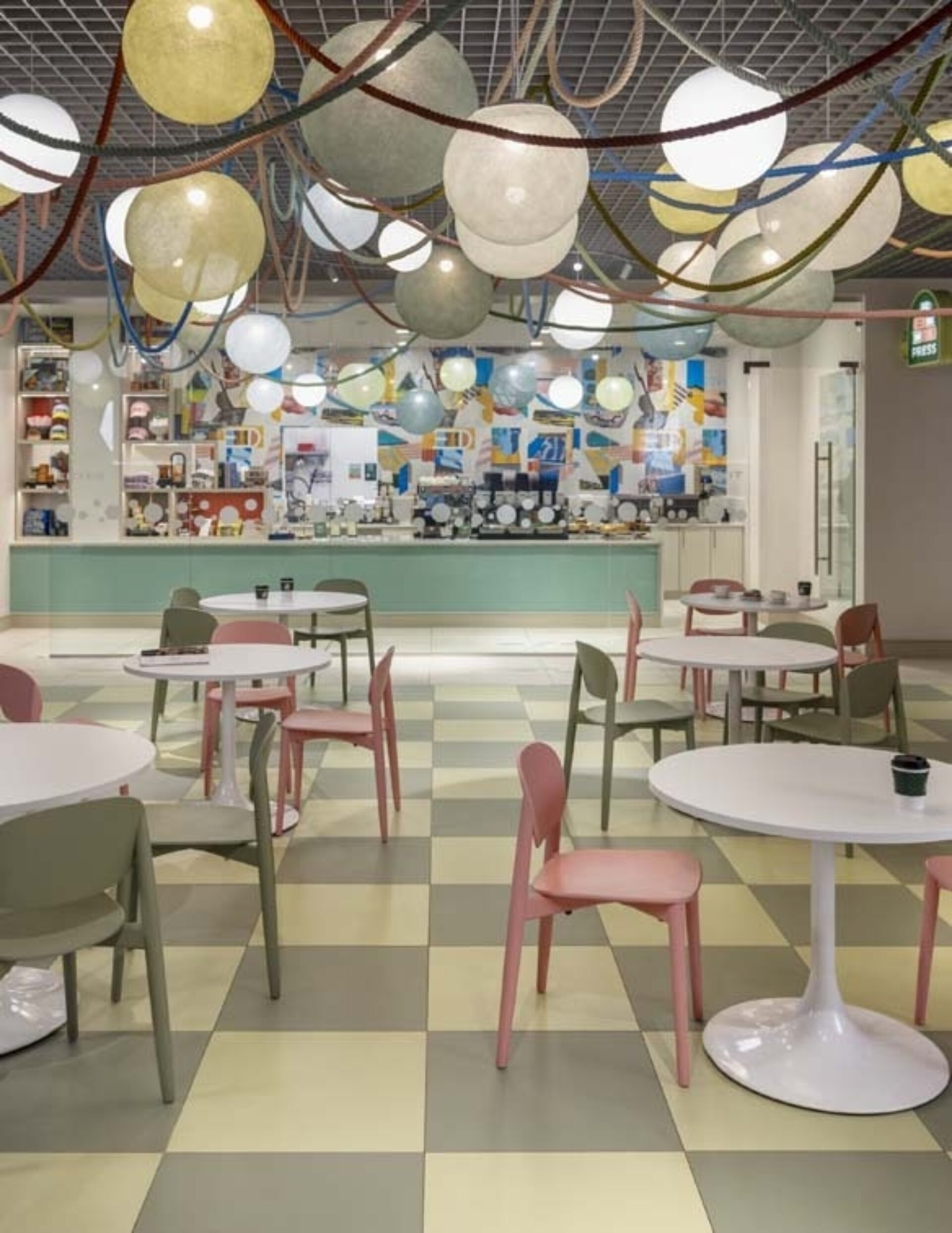 A vibrant café features colorful pendant lights overhead, cheerful furniture, and a bright counter displaying an array of refreshments.