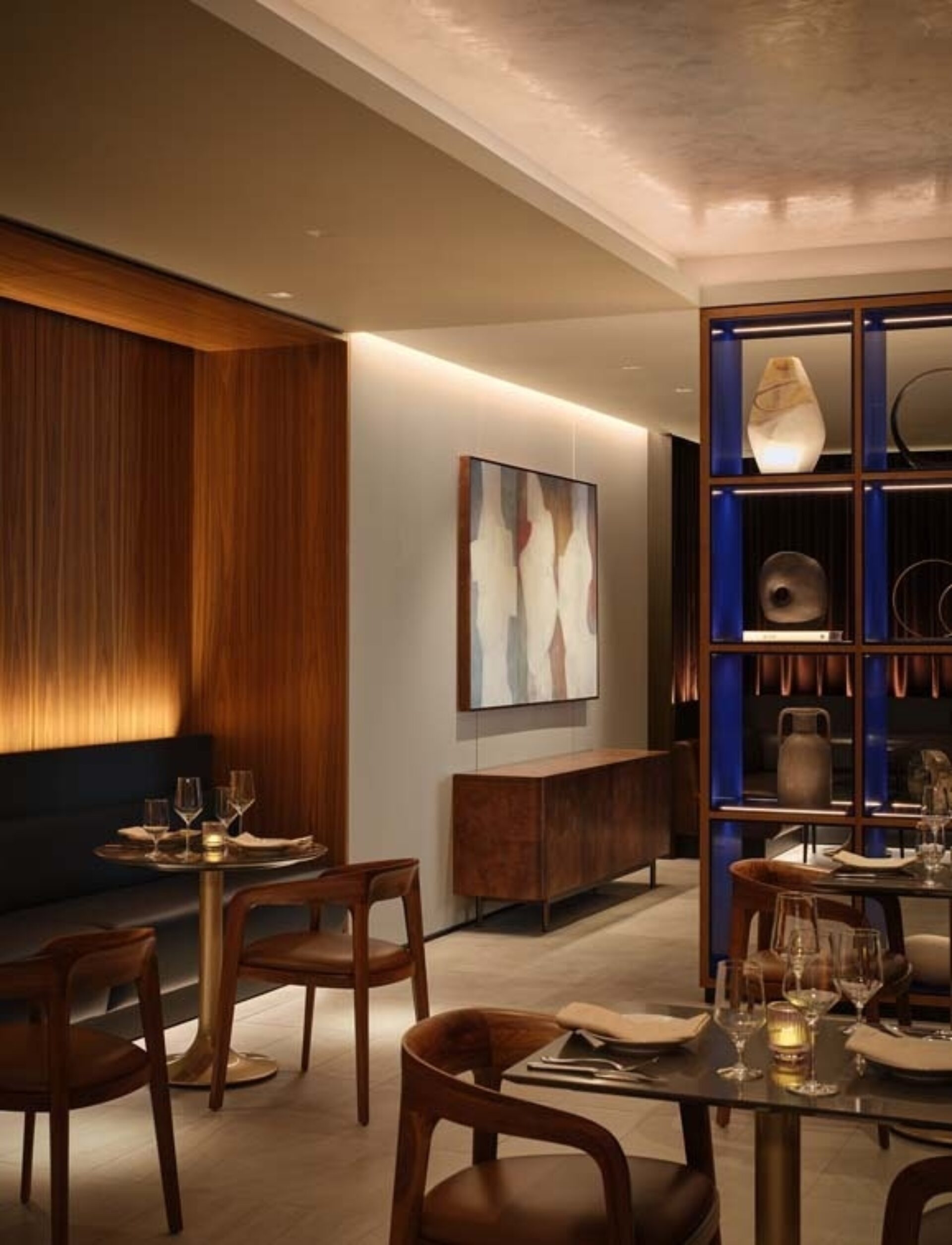 A modern restaurant interior features elegant wooden accents, artistic wall decor, and soft lighting, creating a warm, inviting atmosphere.