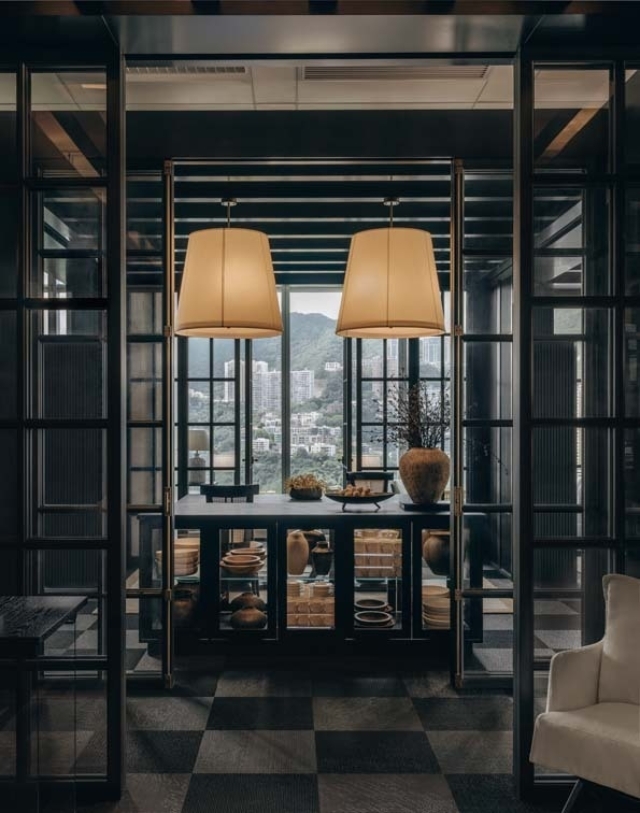 A modern dining space features two large pendant lamps, a dark wood table, decorative pots, and a scenic backdrop of distant mountains.