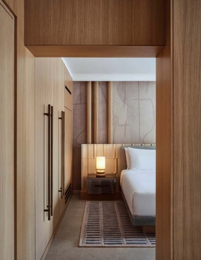 A modern bedroom featuring wooden cabinets, a soft beige palette, a patterned rug, and a stylish lamp beside the neatly made bed.