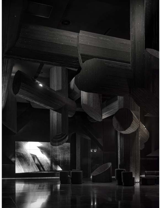 An artistic interior features large, dark abstract wooden structures, complemented by a sleek video screen and low seating.