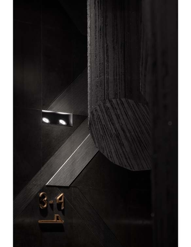 A modern architectural space featuring dark walls, linear textures, and elegant lighting, highlighted by stylish numbers on the wall.