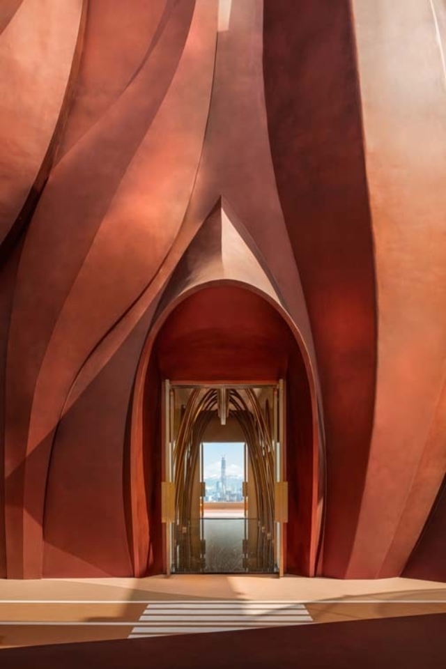 A dramatic interior with flowing, warm-toned walls leading to an inviting glass door that frames a city skyline in the background.