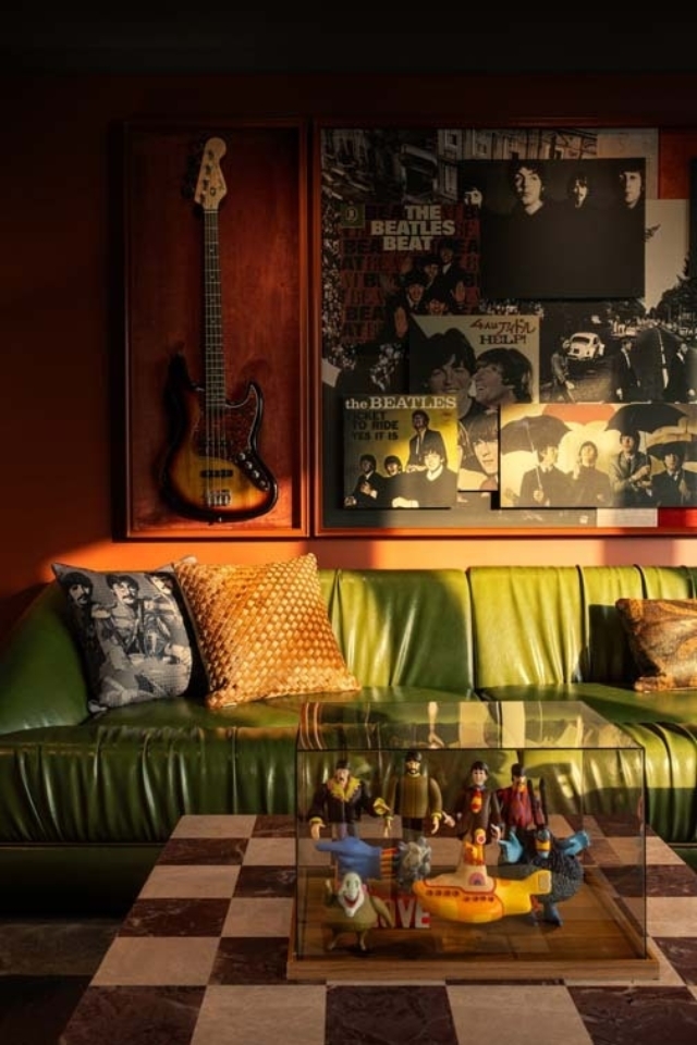 A green leather couch adorned with patterned pillows sits beneath a wall displaying Beatles memorabilia, next to a glass display of figurines.
