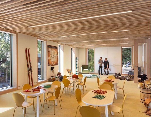 Bright, spacious room with wooden beams, featuring tables and chairs, ski equipment, and two people engaging in conversation.