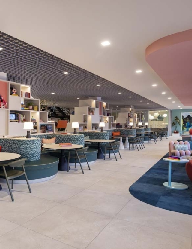 A modern, stylish café interior featuring circular booths, pastel accents, bookshelves, and cozy lighting for a welcoming atmosphere.