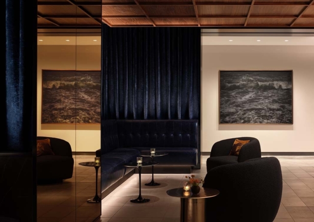 A modern lounge features dark blue curtains, plush seating, and framed artwork of ocean waves, creating an inviting, elegant atmosphere.