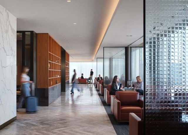 A modern lounge area features sleek furniture, people engaged in conversation, and a stylish separation of space with glass walls.