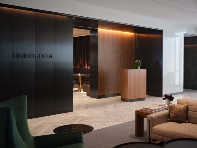 A modern dining room entrance features sleek dark wood panels, a welcoming reception desk, and elegant furniture in neutral tones.