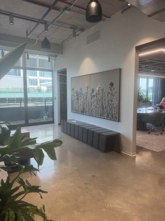 Modern office lobby with polished concrete floor, large glass balcony, mosaic floral wall panel above six black cube benches, potted plants.