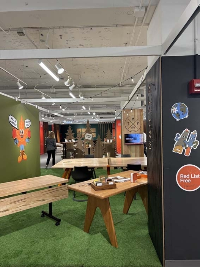 Open showroom with green turf floor, wooden tables and benches, cartoon wall art, stickers on a dark pillar, and a person walking away.