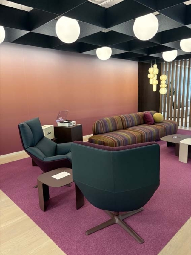 Modern lounge with a magenta carpet, striped multicolored sofa, teal swivel chairs, round globe ceiling lights, pendant cluster, turntable.