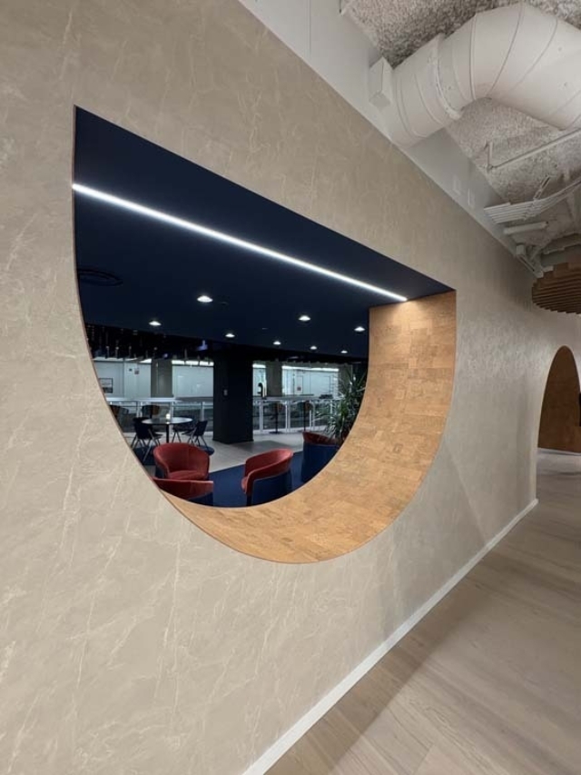 Curved wall opening reveals modern lounge with red armchairs, navy ceiling with LED strip, railing and exposed ductwork.