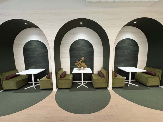Three arched alcove booths with olive-green seats, white pedestal tables, dark textured back panels, burgundy bolsters, floral centerpiece.