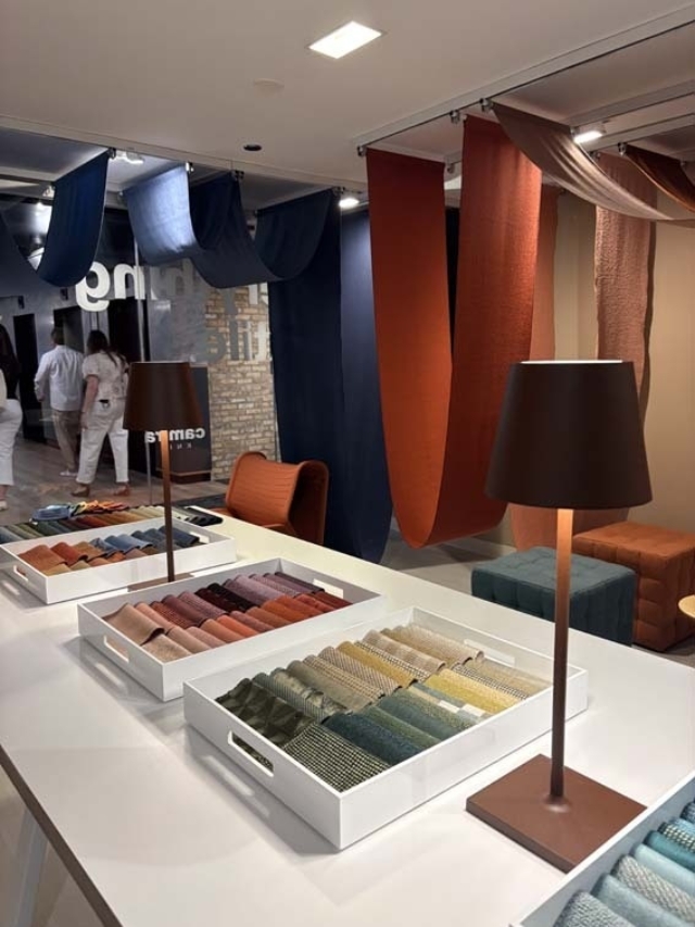 Showroom table with organized fabric swatch trays and rust and navy draped panels overhead, brown lamps and upholstered seats visible.