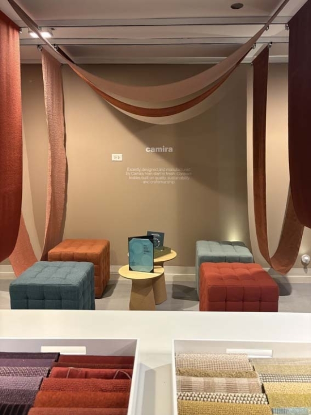Showroom with rust and terracotta fabric swags suspended above teal, orange and red tufted ottomans, small tables and fabric sample trays.