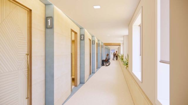 A brightly lit hallway features numbered doors, with a person in a wheelchair and others walking, surrounded by indoor plants.