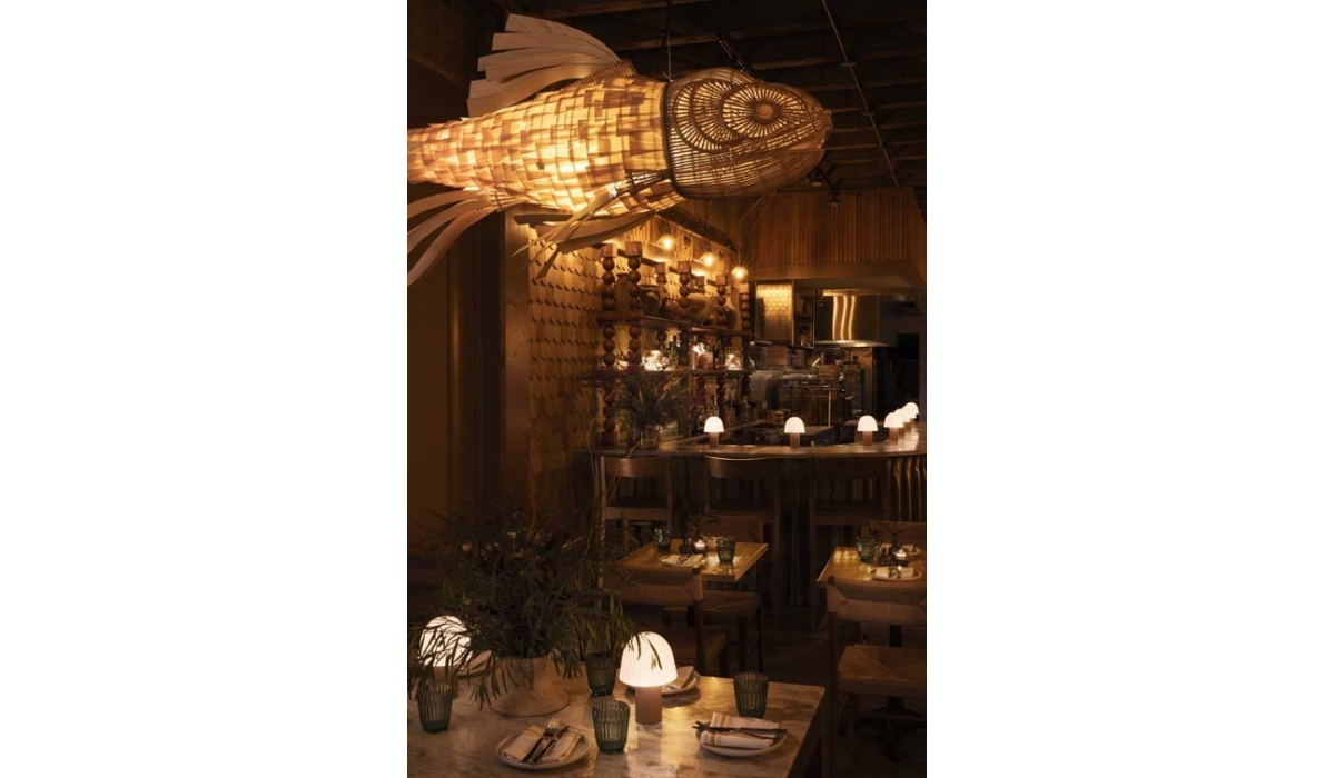 A lavish restaurant interior features a large, woven fish lantern hanging above a stylish bar, with dim lighting and elegant decor.