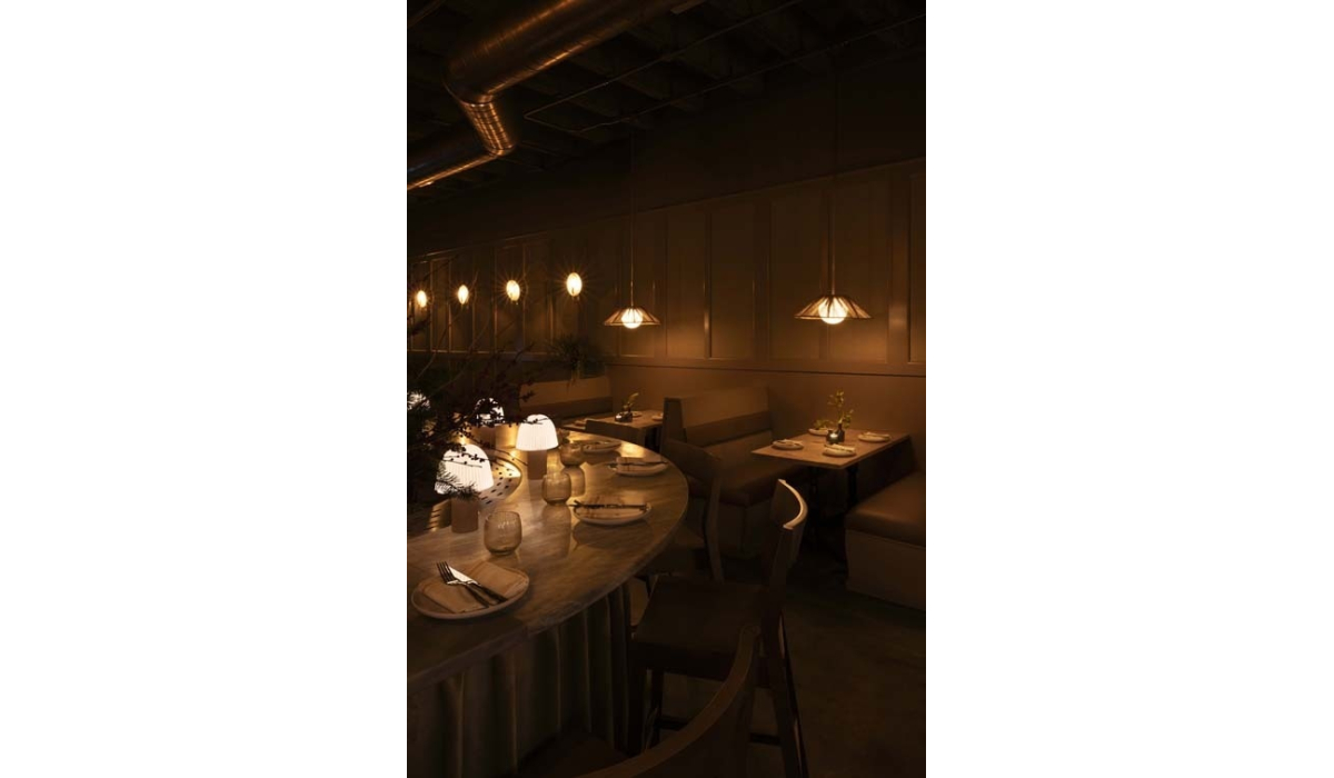 A stylish restaurant interior features softly lit tables with elegant lamps, creating a cozy atmosphere for dining. Decorative plants add charm.