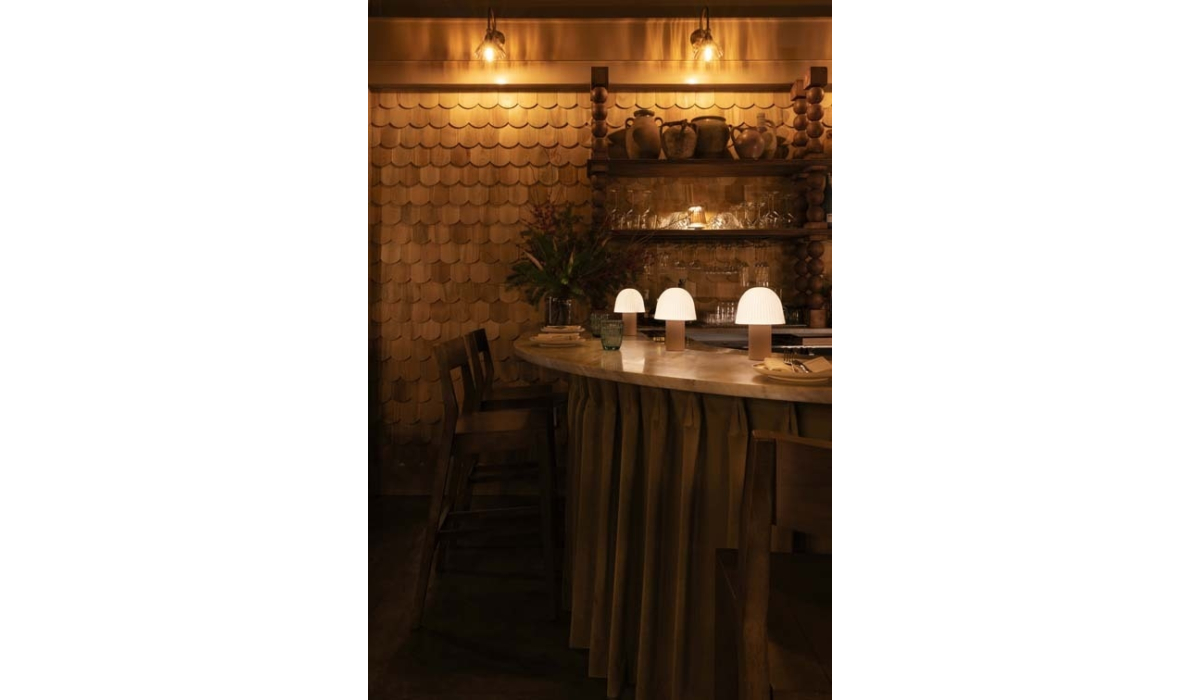 Soft, warm lighting casts a cozy glow over a bar with elegant decor, featuring round lamps, wooden shelves, and inviting seating.