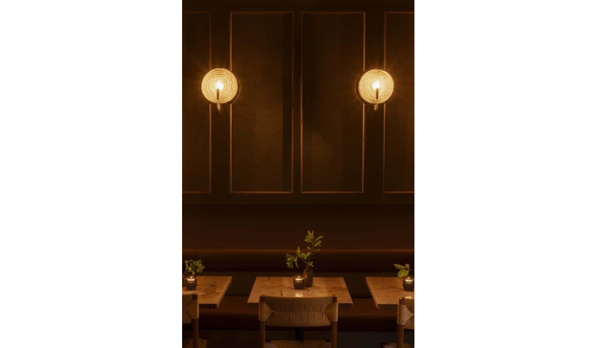 Warmly lit dining area featuring wooden tables adorned with small plants and elegant candle holders against dark walls.