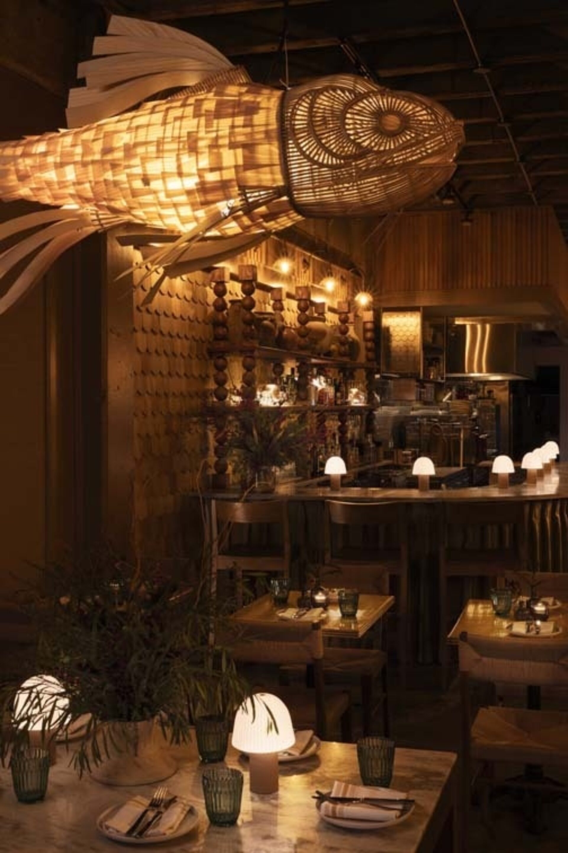 A lavish restaurant interior features a large, woven fish lantern hanging above a stylish bar, with dim lighting and elegant decor.