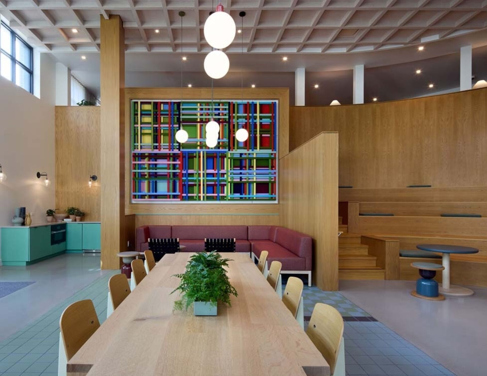 Bright, modern interior featuring a long wooden table, colorful wall art, cozy seating areas, and vibrant decor elements.