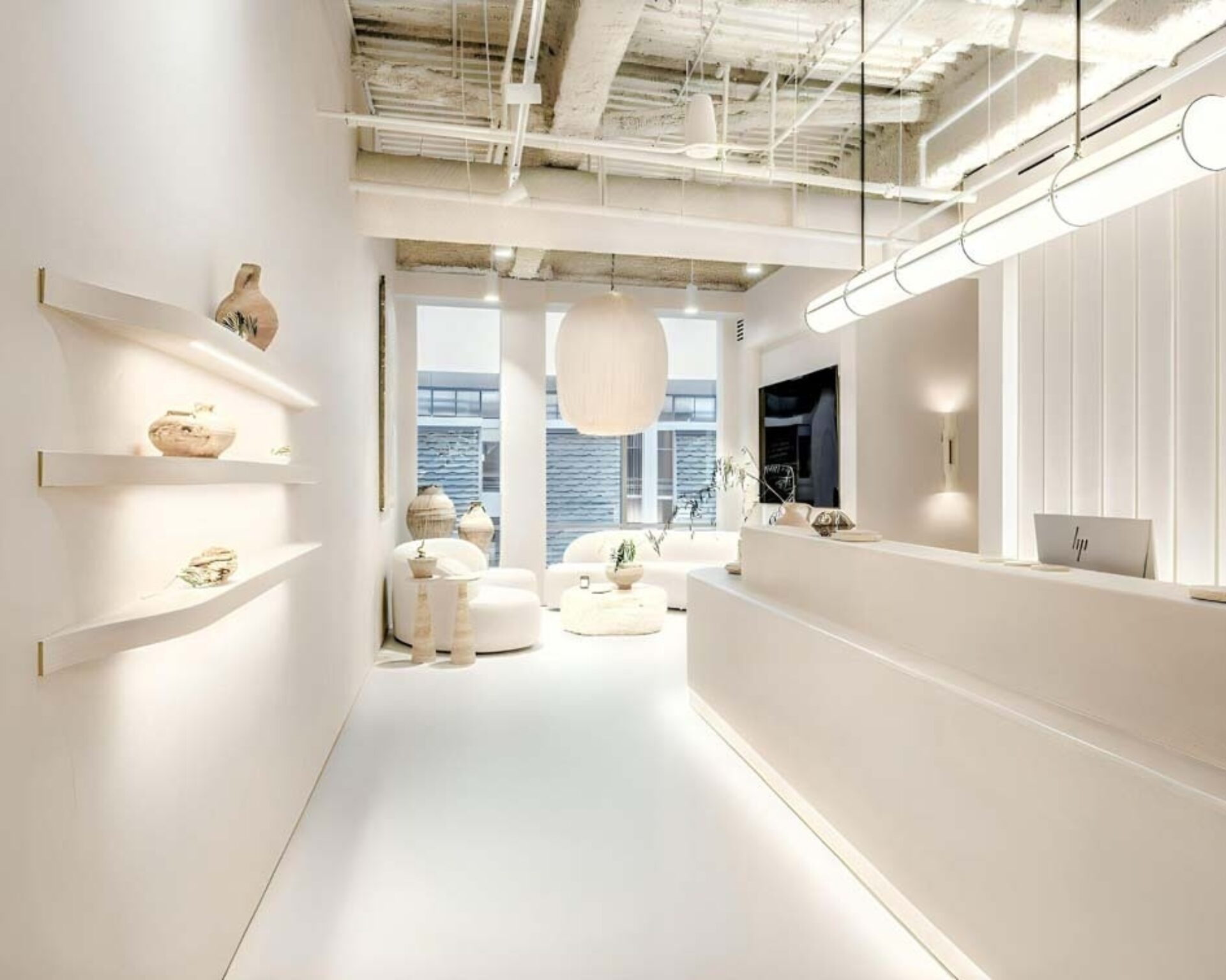 A modern reception area featuring white walls, soft lighting, minimalist furniture, and decorative pottery on sleek shelves.