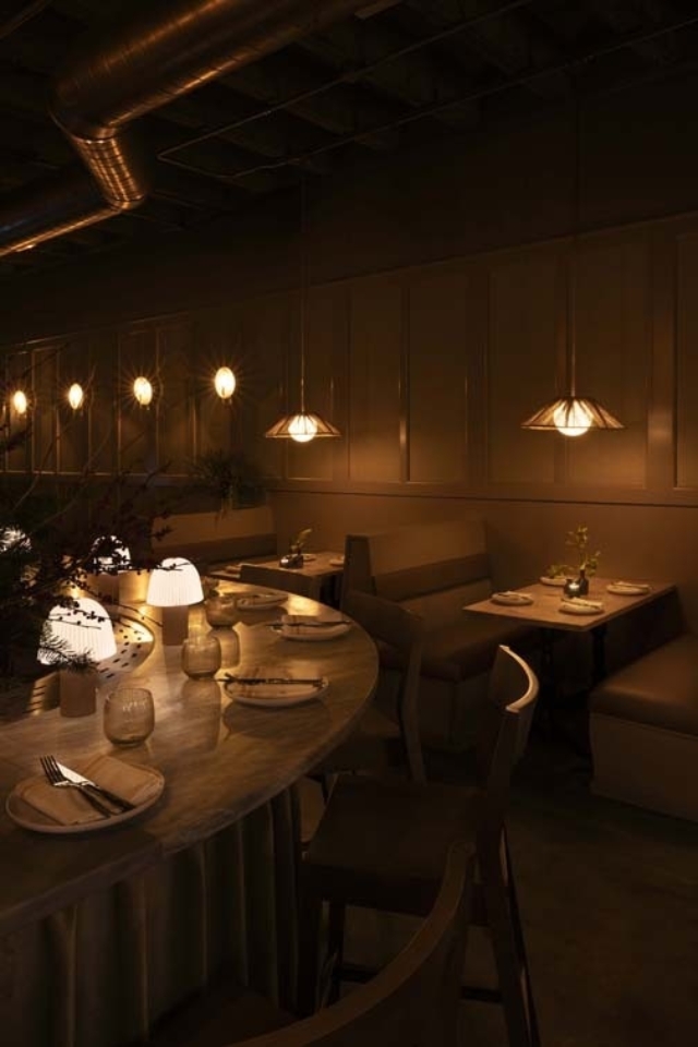 A stylish restaurant interior features softly lit tables with elegant lamps, creating a cozy atmosphere for dining. Decorative plants add charm.