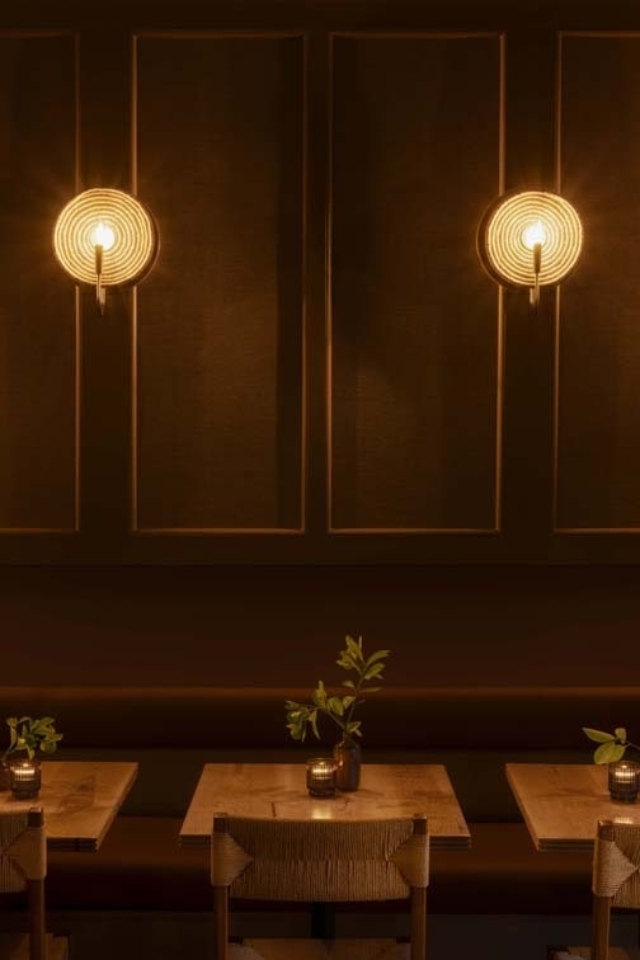 Warmly lit dining area featuring wooden tables adorned with small plants and elegant candle holders against dark walls.