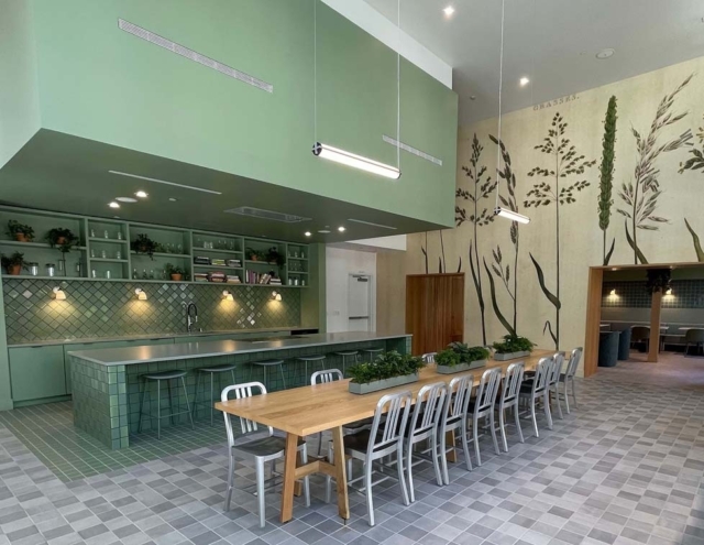 A modern kitchen and dining area featuring green cabinetry, a large wooden table, and decorative plant motifs on the walls.