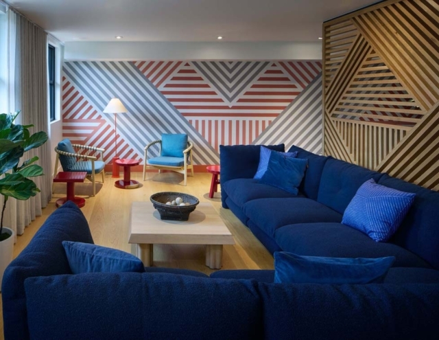 A stylish living room featuring a navy sofa, colorful accent chairs, a wooden coffee table, and a vibrant striped wall design.
