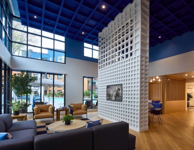 A spacious modern lobby features a striking blue ceiling, large windows, a unique white patterned wall, and cozy seating areas.