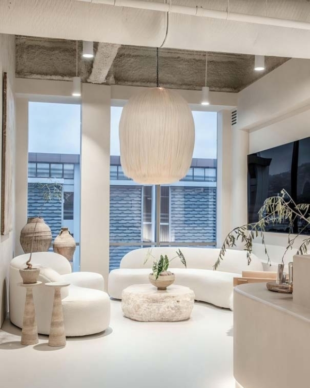 A modern living space features curved white furniture, large windows, and a distinctive hanging lamp, creating a bright, airy atmosphere.