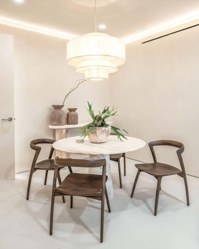 A modern dining area features a round table, four wooden chairs, a large pendant light, and potted plants, creating a cozy ambiance.
