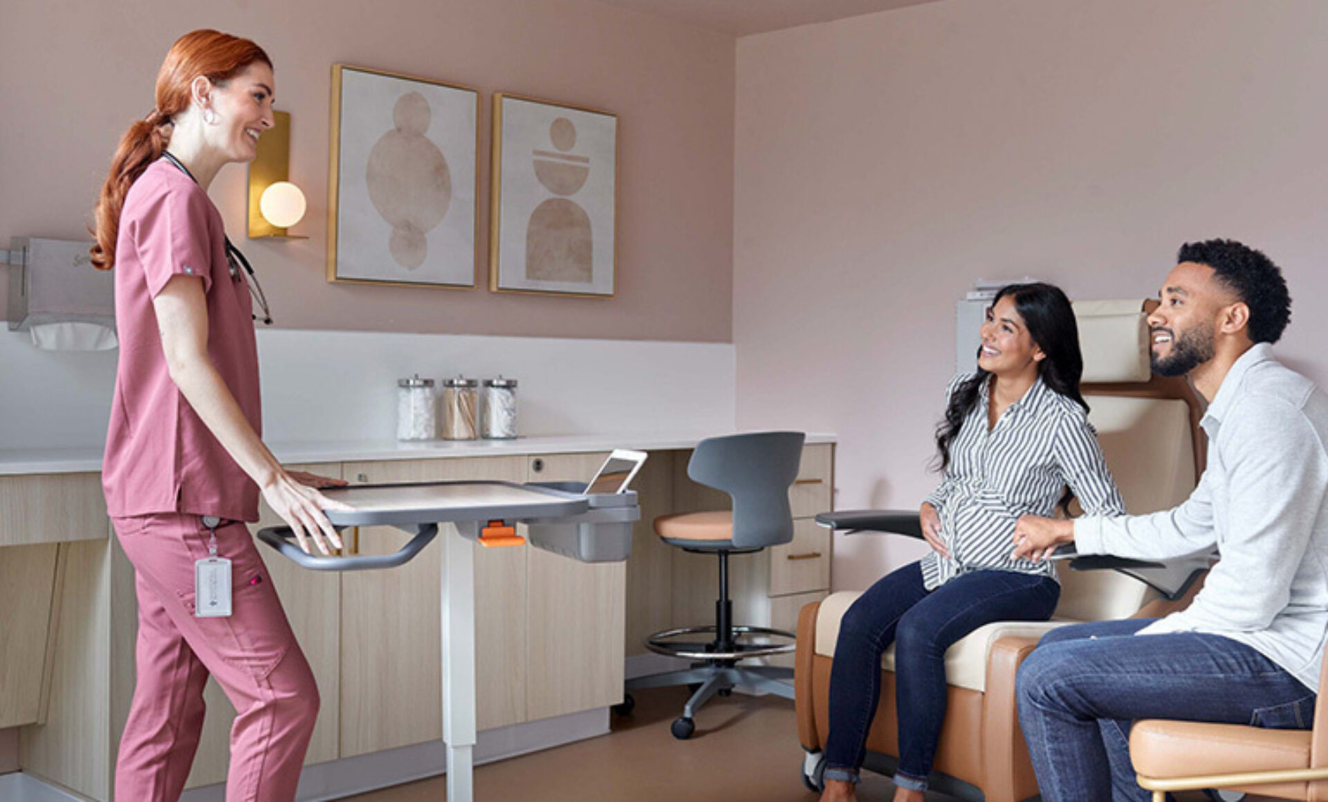 A healthcare professional in scrubs smiles while communicating with a couple in a warmly decorated clinic room, preparing for consultation.