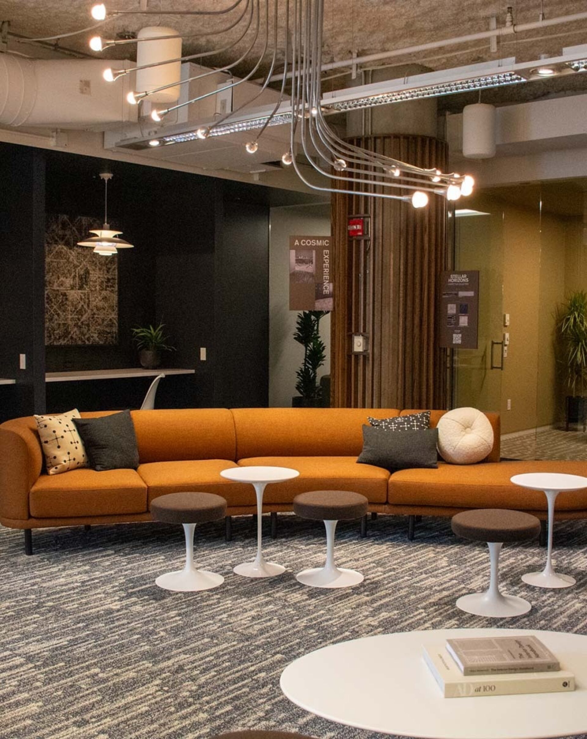 A modern lounge area features an orange sectional sofa, small white tables, and decorative accents, creating a stylish and inviting space.