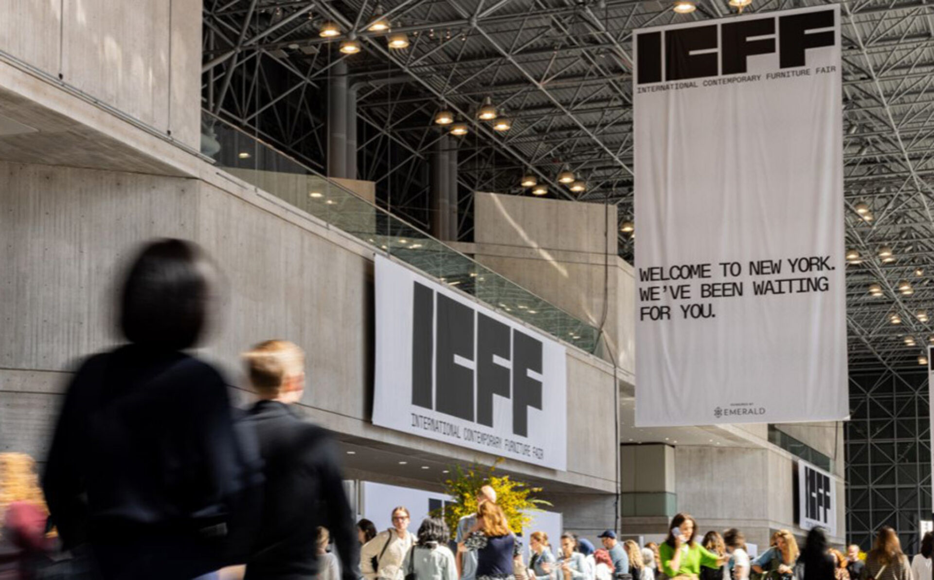 Crowds bustle in a modern venue adorned with banners for the International Contemporary Furniture Fair, welcoming attendees to New York.