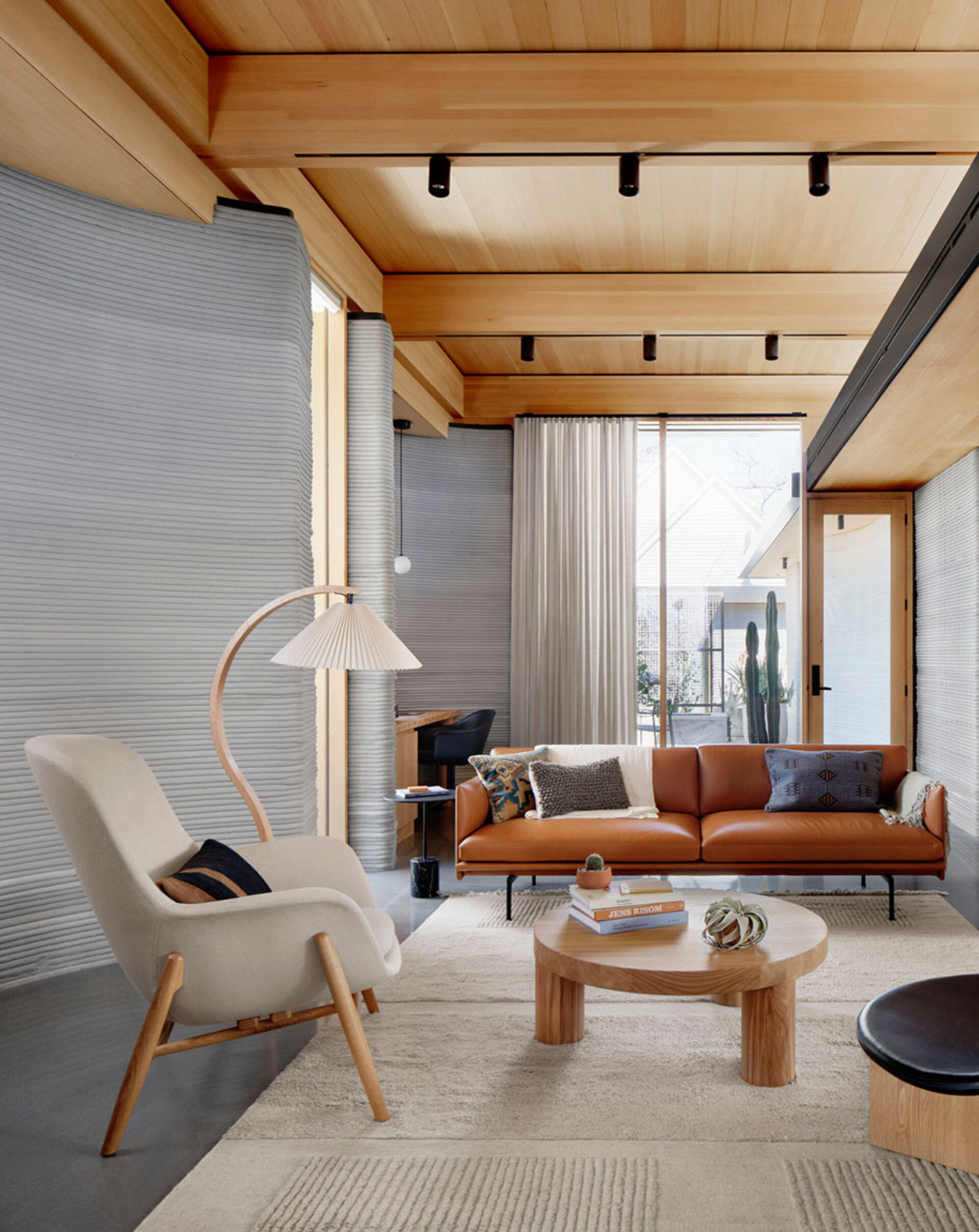 A modern living room featuring a leather sofa, plush armchair, wooden coffee table, and elegant lamps, with natural light streaming through large windows.