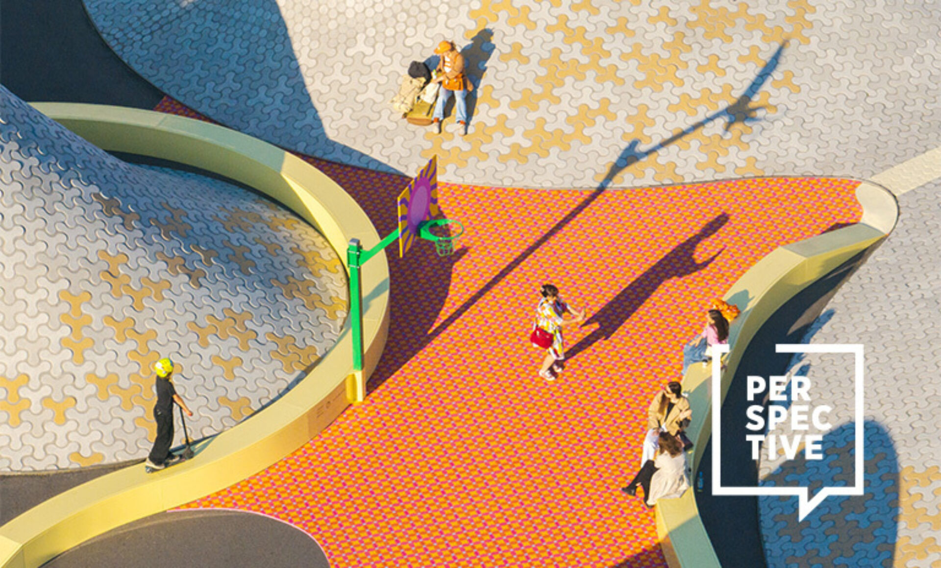 Aerial view of a colorful urban plaza with curving yellow walkways, patterned tiles, scattered pedestrians, a scooter rider and long shadows.