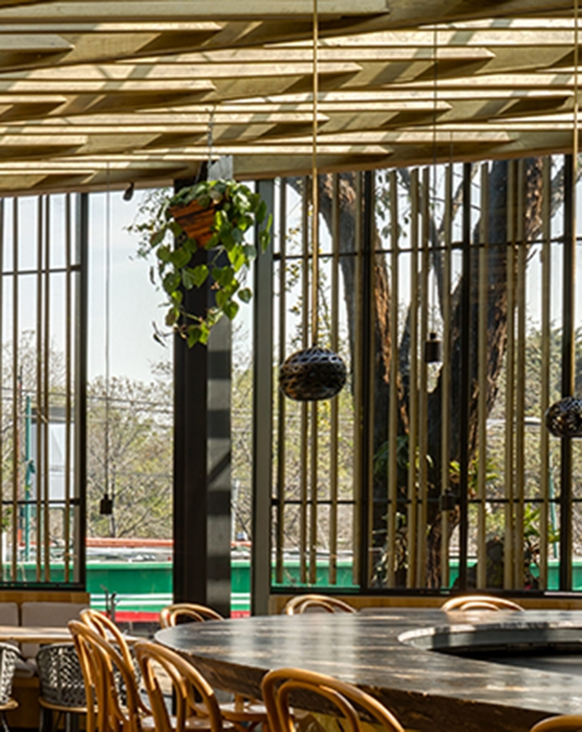 A spacious dining area features a large wooden table surrounded by stylish chairs, with hanging plants and sunlight filtering through large windows.