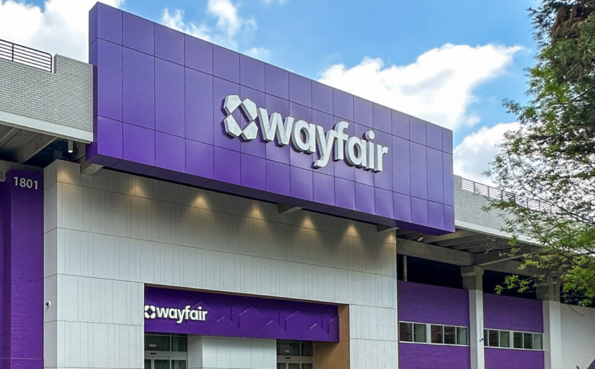 The Wayfair store features a prominent purple facade with the brand name displayed in white, surrounded by trees and a cloudy sky.