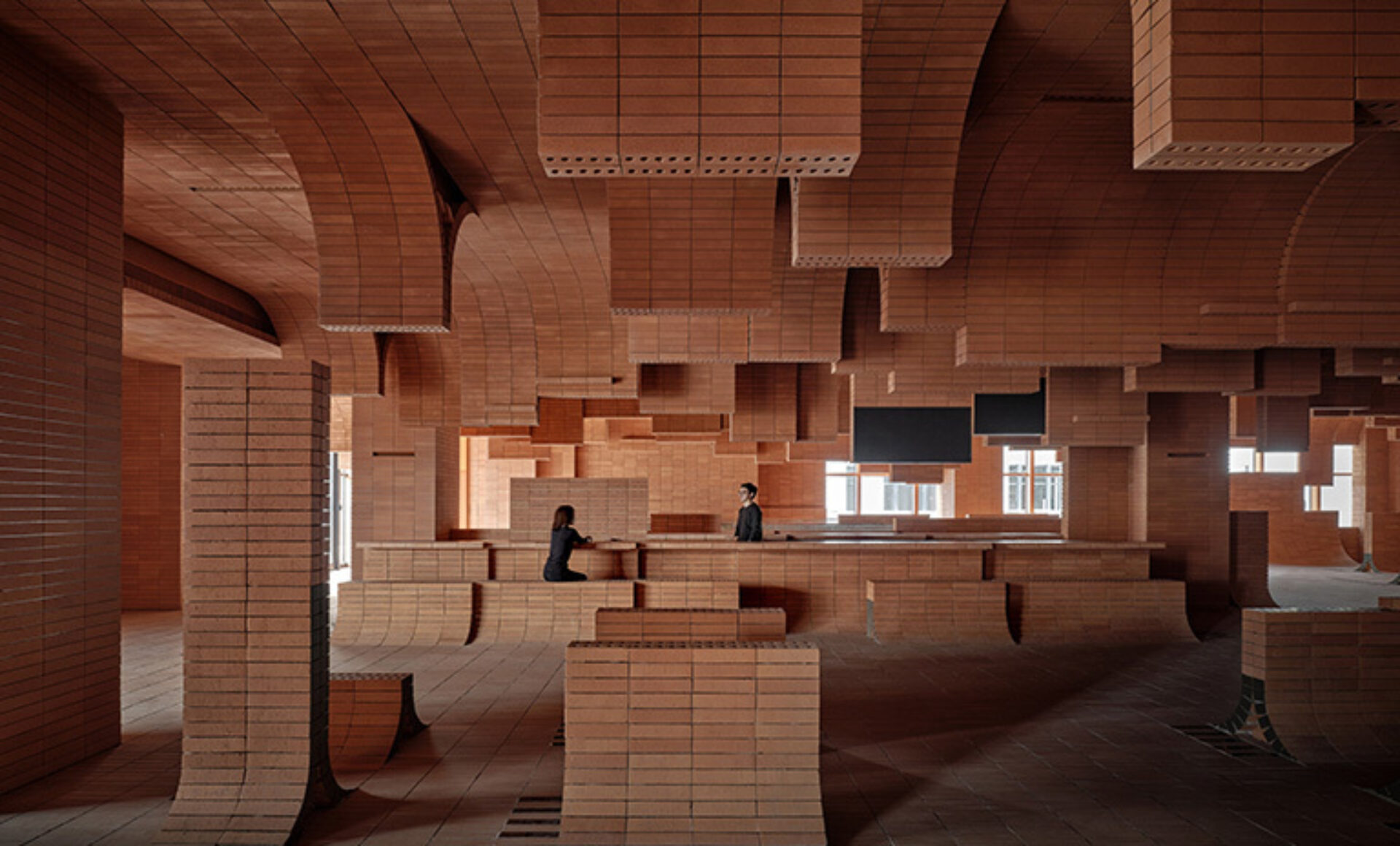 An innovative architectural space features curved, terracotta brick structures with two people engaged in conversation amidst the unique design.