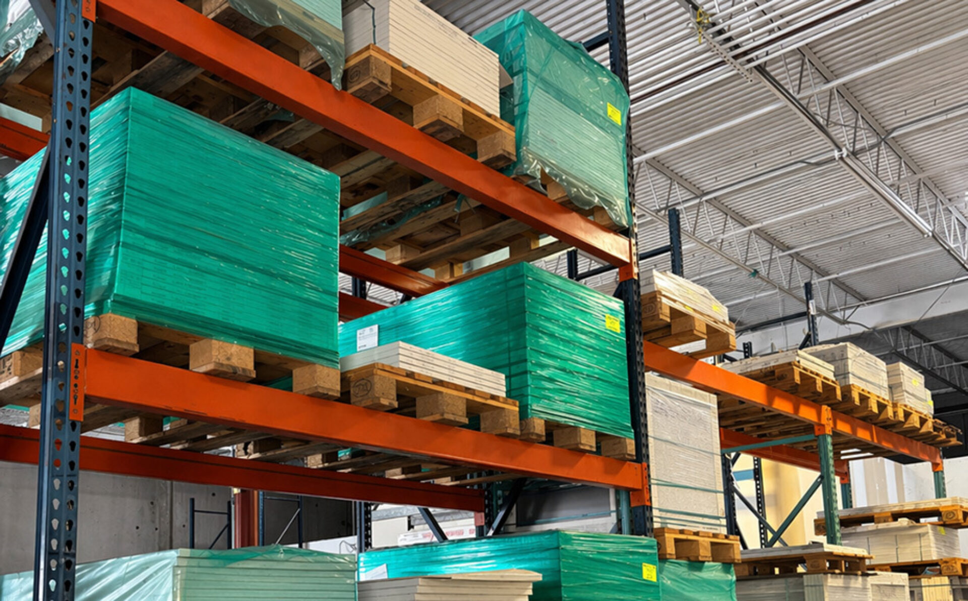 Stacks of brightly colored pallets of materials are neatly organized on metal shelving in a well-lit warehouse setting.