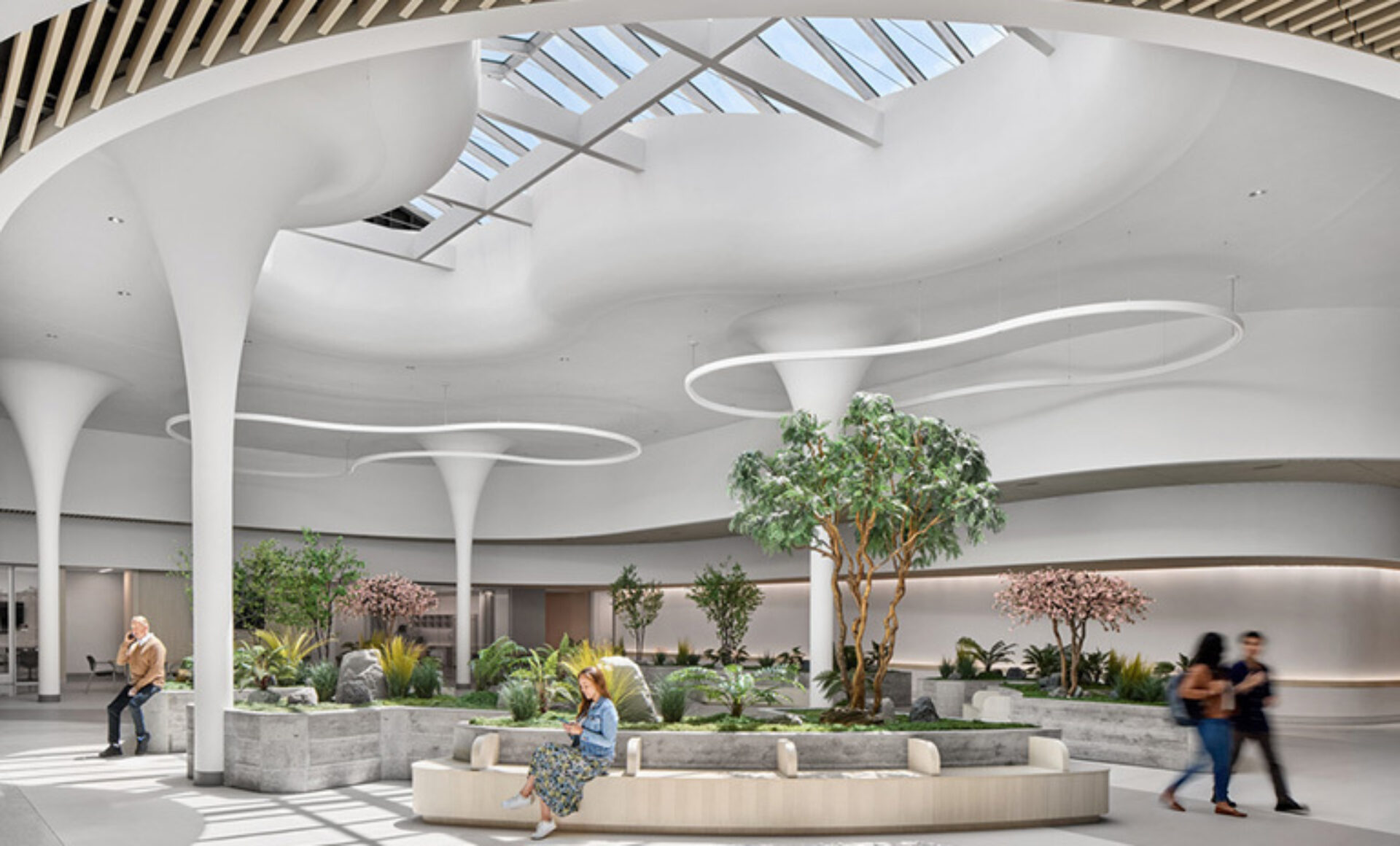 A spacious, modern atrium features sleek white pillars, abundant greenery, and natural light from a skylight, creating a serene atmosphere.